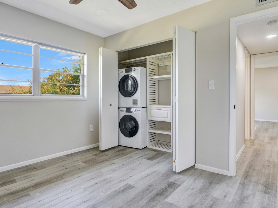 A room with a window and a large closet with a stacked washer and dryer and storage shelves inside.